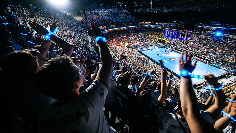 Ausverkaufte Handballarena mit jubelnden Fans während eines Spiels.