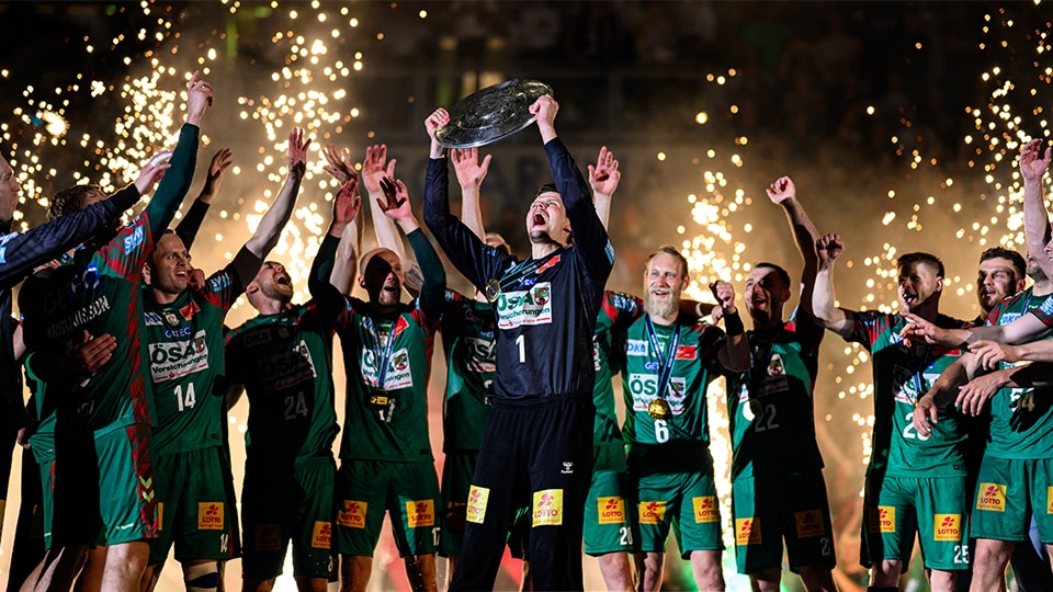 Handballspieler beim Sprungwurf während eines Spiels vor voller Arena.