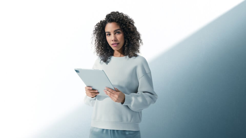 Frau hält ein graues Tablet vor einem grauen und weißen Hintergrund.
