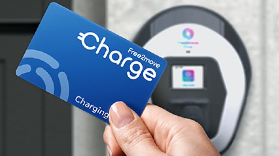 Hand, die eine blaue Free2Move Charge kontaktlose Karte in die Nähe einer Elektrofahrzeug-Ladestation hält.