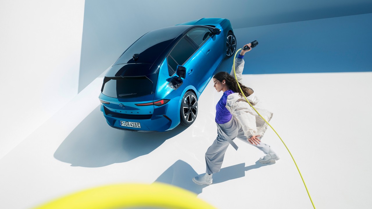 Draufsicht auf einen blauen Opel Astra Electric mit schwarzem Dach und einer Frau, die einen gelben Ladekabel herumwirbelt